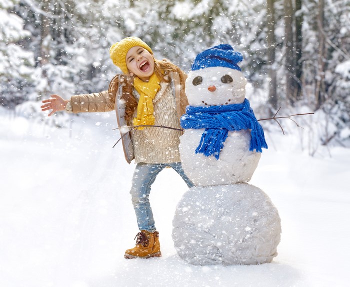 Girl in winter clothes with a snowman