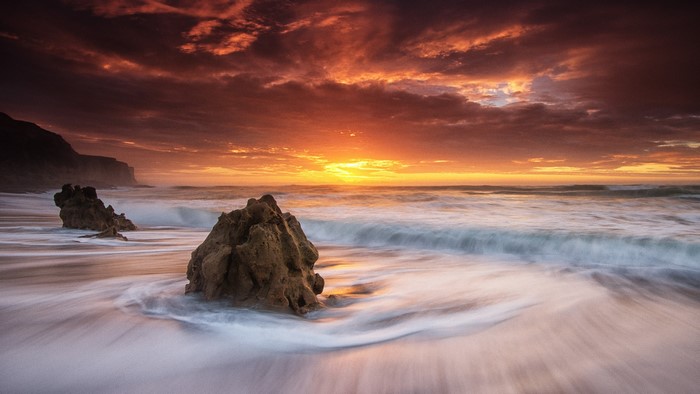 Sunset over the ocean with rocks on the shore