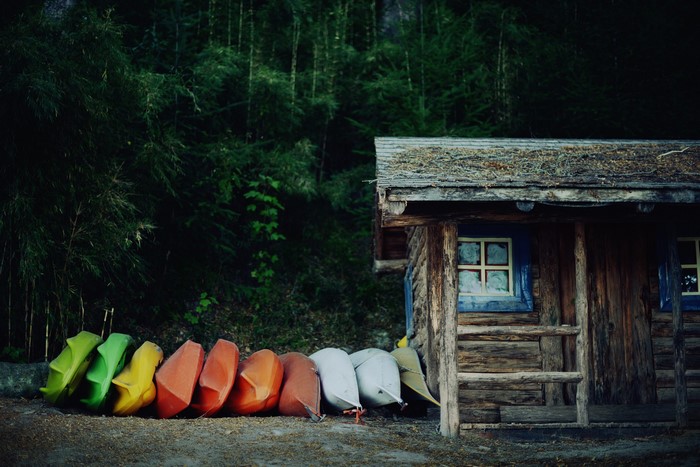 Colorful kayaks lined up next to a rustic wooden cabin