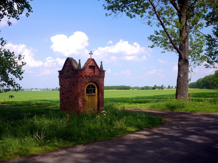 Brick wayside shrine with a cross in a green field
