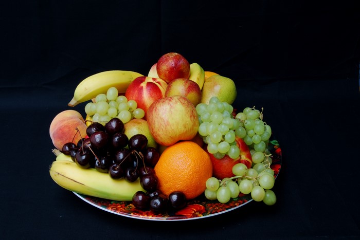 A fruit bowl filled with grapes, apples, cherries, bananas, peaches, and an orange
