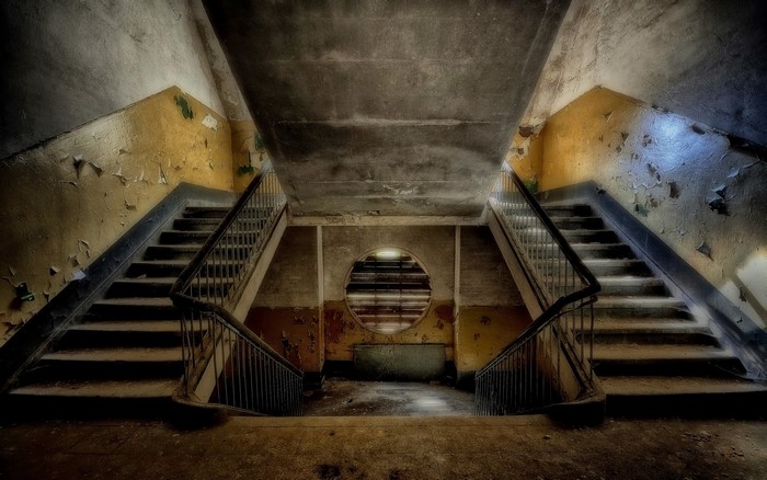 Abandoned building interior with decaying stairs and circular window