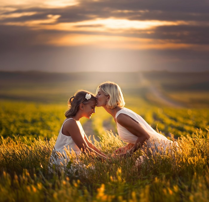 Mother kissing daughter in a field at sunset