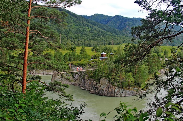 Suspension bridge connecting rocky island with buildings in a forested mountain landscape