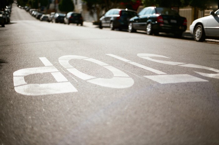 Stop sign painted on asphalt road with cars parked