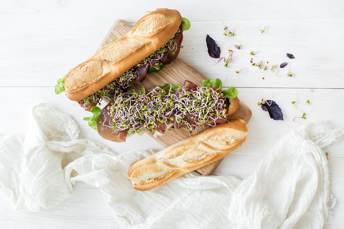 Two sandwiches with sprouts and ham on a wooden board