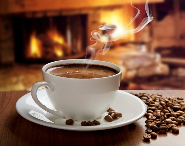 Cup of Coffee with Steam and Coffee Beans by Fireplace