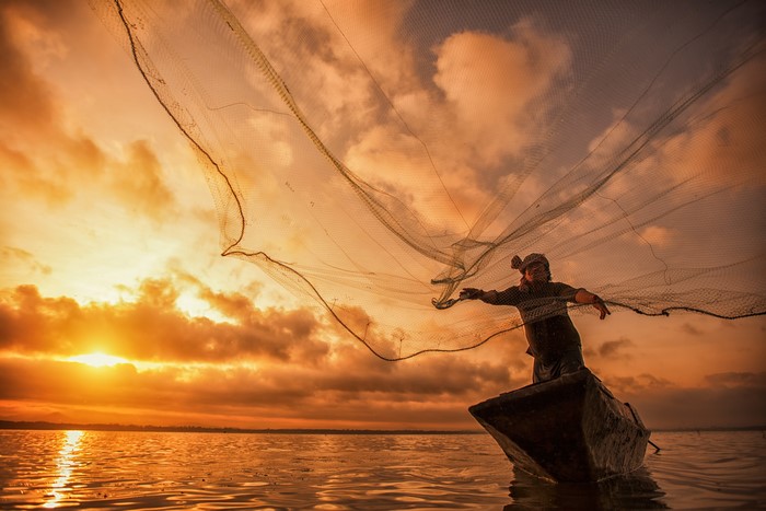 Fisherman casting net from boat at sunset