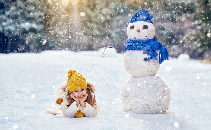 Girl in yellow hat with snowman in winter