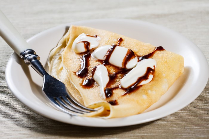 Pancake with cream and chocolate sauce on a plate with a fork