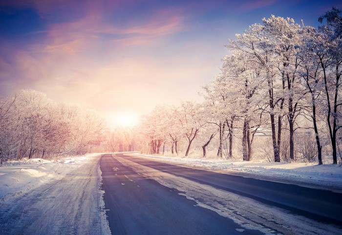 Winter road with snow-covered trees at sunrise