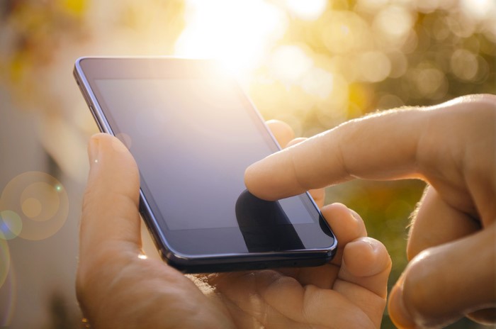 Hands holding a smartphone in sunlight