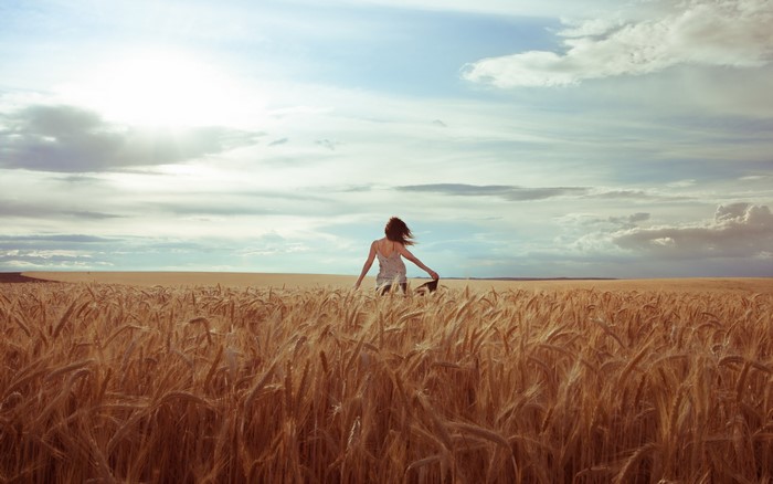Woman running through a wheat field under a cloudy sky
