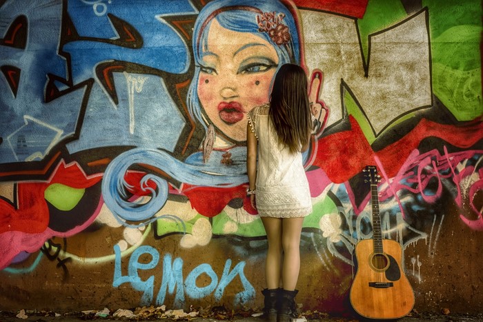 Girl in white dress standing in front of graffiti with guitar