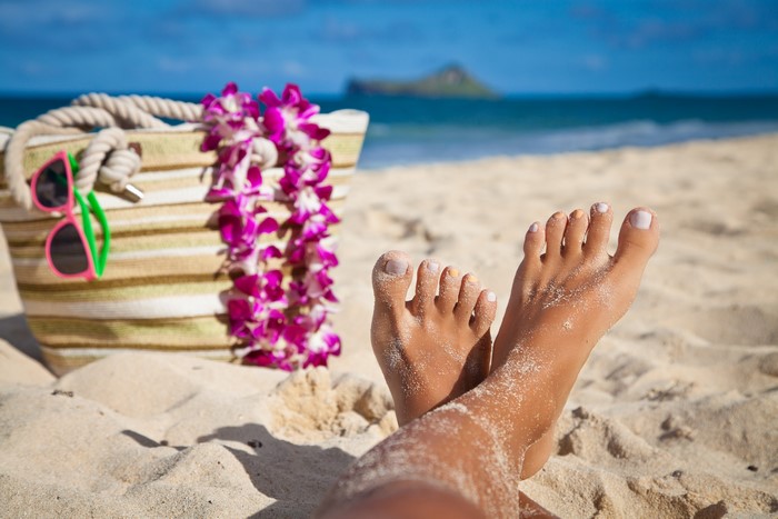 Legs on a sandy beach with a bag and lei