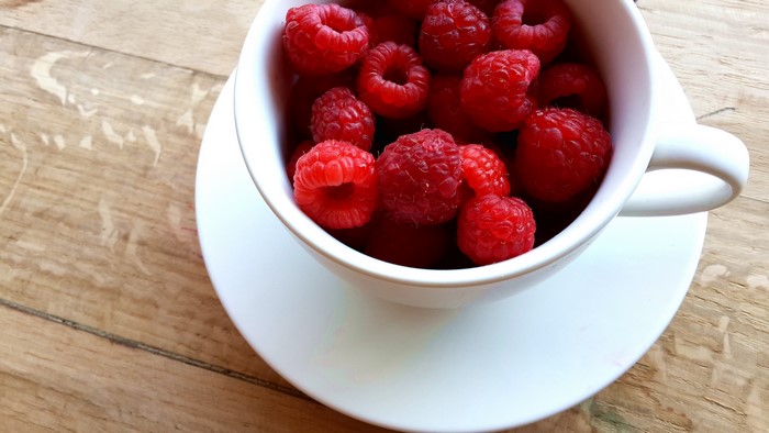 Raspberries in a white cup and saucer