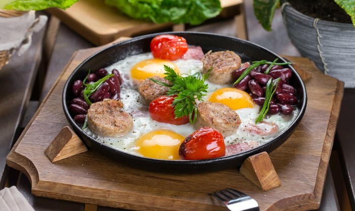 Fried eggs with sausages, tomatoes, and beans in a frying pan