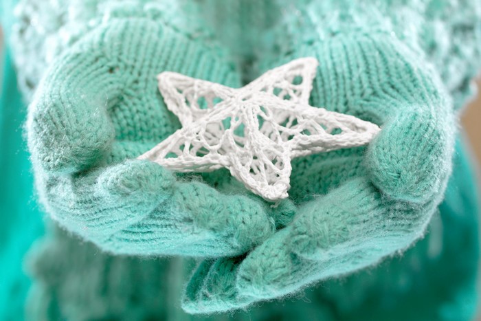 Hands in mint green knitted gloves holding a white star ornament
