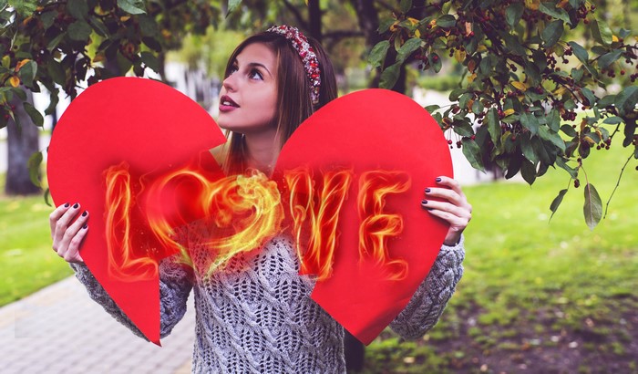 Woman holding a broken heart with burning 'LOVE' text