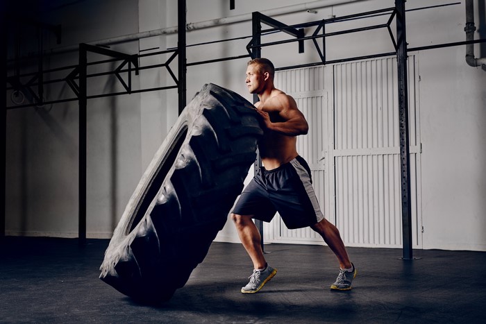 Man flipping a large tire in a gym