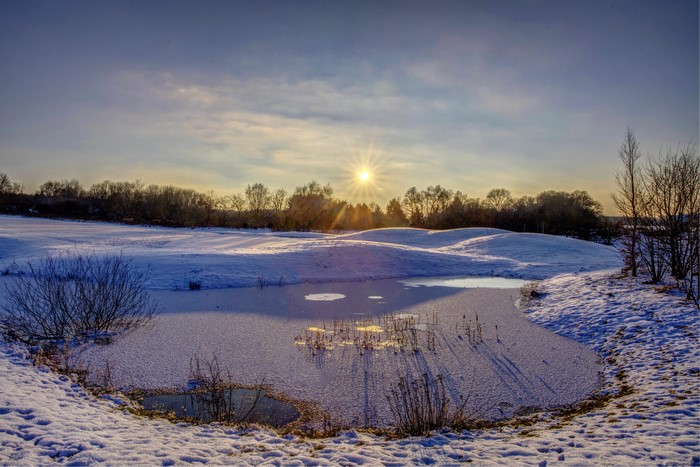Winter sunrise over a snowy landscape with a frozen pond