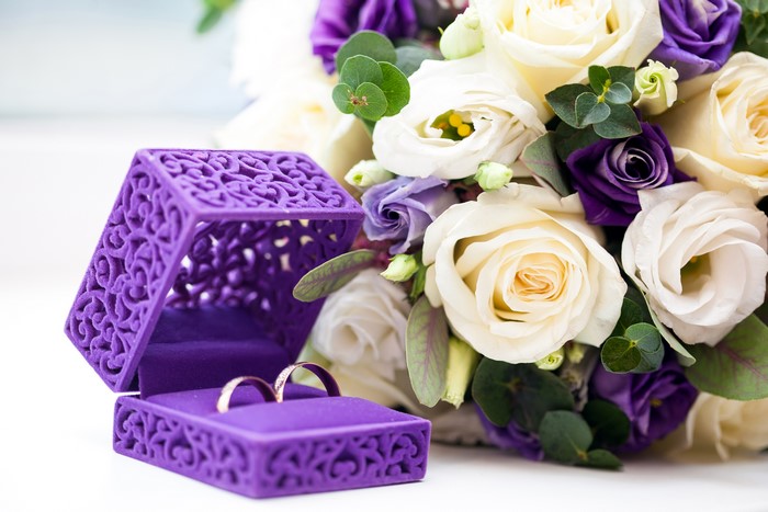 Wedding rings in a purple box with a bouquet