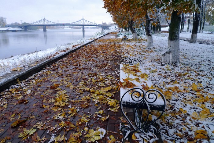 Autumn snow on the Volga River waterfront with a bridge and bench