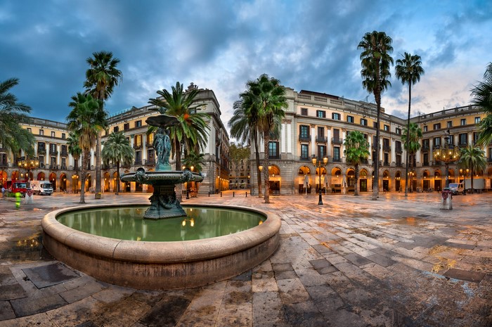 Fountain in a square with palm trees and buildings in Barcelona