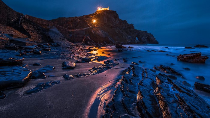 Coastline at night with illuminated building on cliff