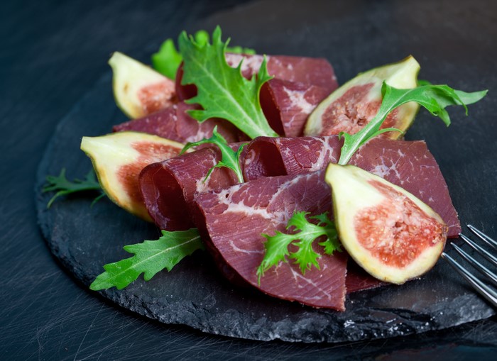 Cured meat with figs and greens on a slate plate