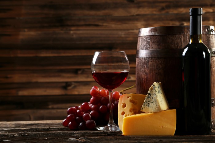 Wine bottle, glass, grapes, cheese, and barrel