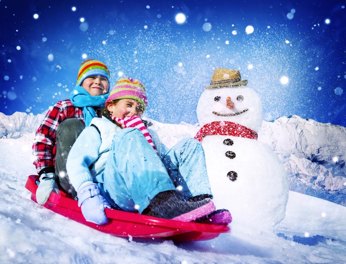 Children sledding with a snowman