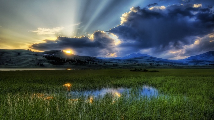 Sunbeams over a grassy field and lake at sunset