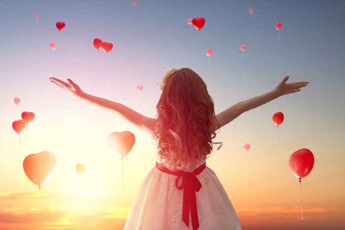 Girl releasing heart balloons at sunset