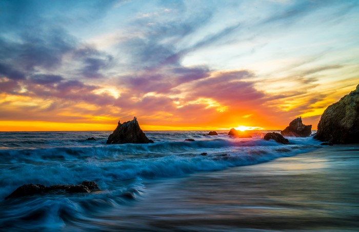 Sunset over the ocean with waves and rocks at Malibu, USA