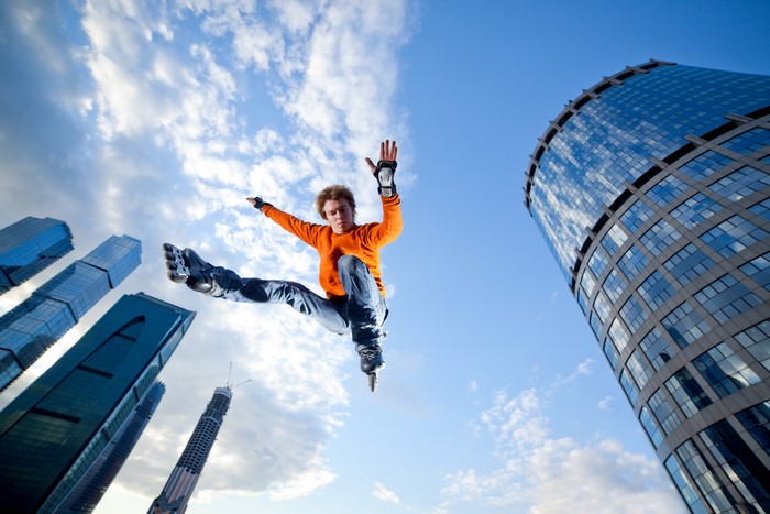 Man in orange sweater jumps on rollerblades with skyscrapers in background