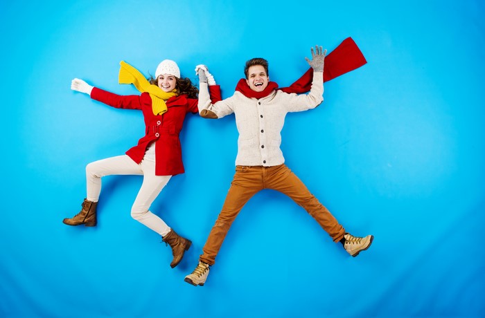 Couple in Winter Clothes Jumping on Blue Background