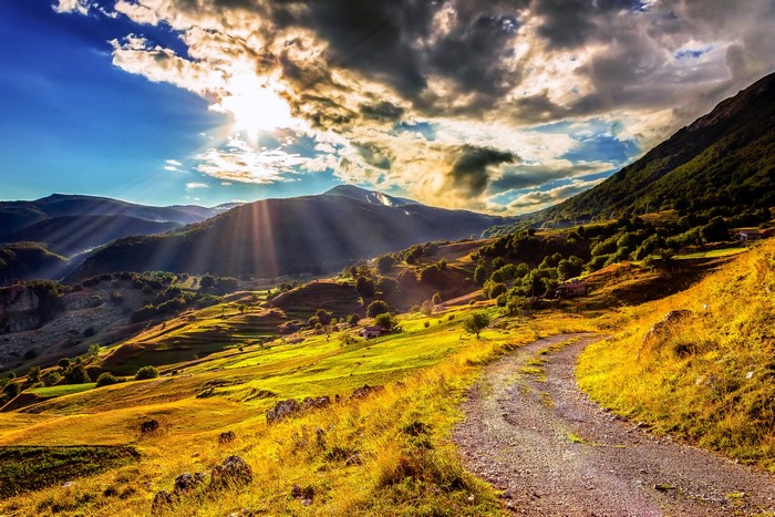 Sunlight beams over a mountain valley with a dirt road