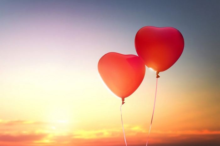 Two red heart balloons against a sunset sky
