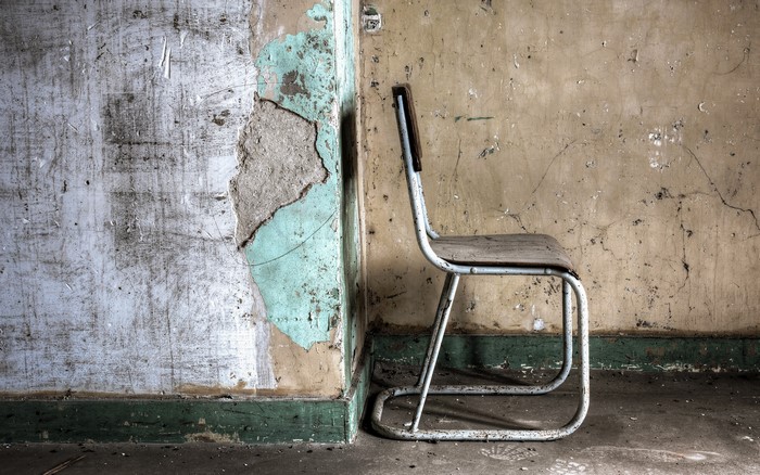 Abandoned chair against a cracked wall