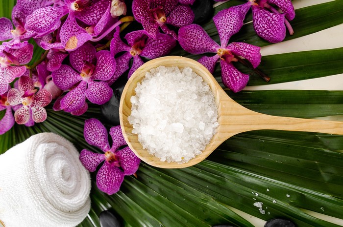 Spa setting with orchids, salt, towel, and palm leaves