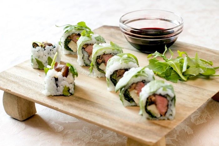 Sushi rolls with meat and greens on a wooden board