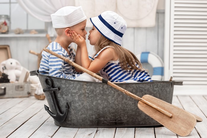 Two children in sailor outfits kissing in a boat
