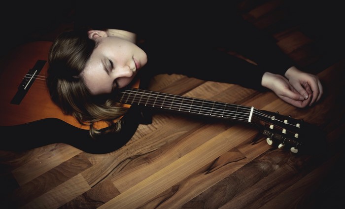Woman sleeping on a guitar on parquetry