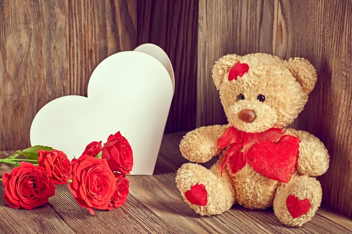 Teddy bear with roses and heart on wooden background