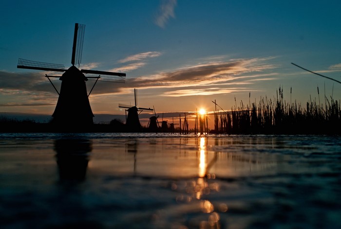 Windmills silhouetted against a sunset over water