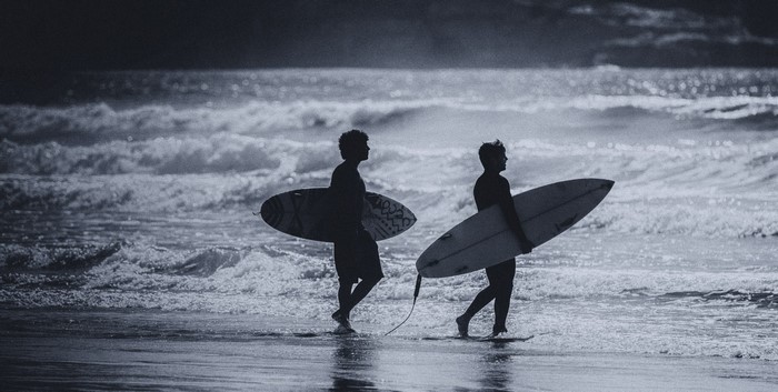 Two surfers walking on the beach with surfboards