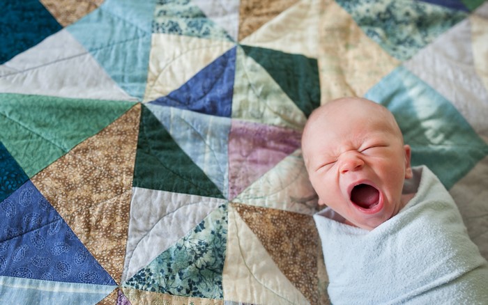 Newborn baby yawning on a colorful quilt
