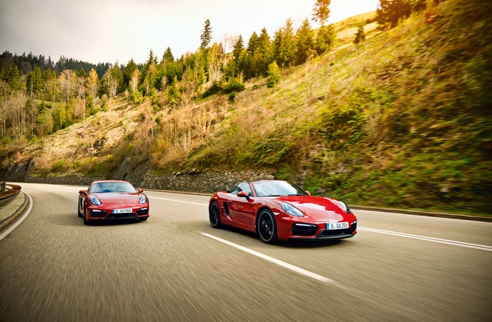 Two red Porsche cars driving on a mountain road
