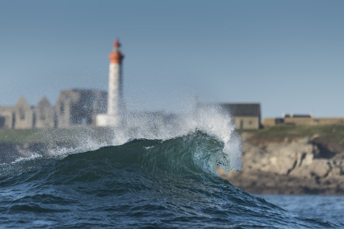Wave crashing in front of a lighthouse and ruins